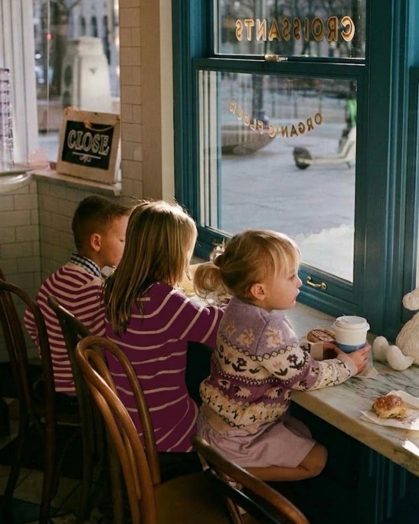 Three children sitting at a cafe window counter with drinks and pastries